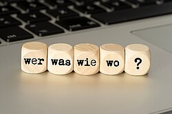 Würfel mit Aufschrift Wer, Was, Wie, Wo, ? auf Tastatur