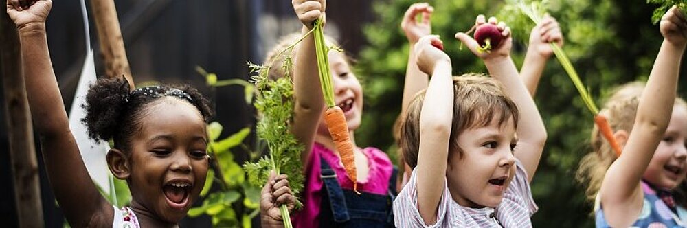 Kinder freuen sich und halten Gemüse hoch